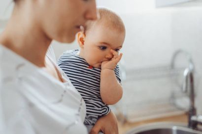 Eine Mutter hält ihr kleines Kind auf dem arm, welches am Daumen lutscht