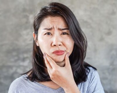 Eine Frau hält ihren schiefen Kiefer fest und verzieht schmerzend das Gesicht