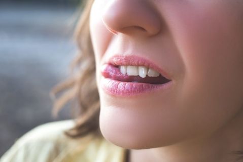 Frau mit einem starken Engstand der Zähne fährt sich mit der Zunge über die Zähne